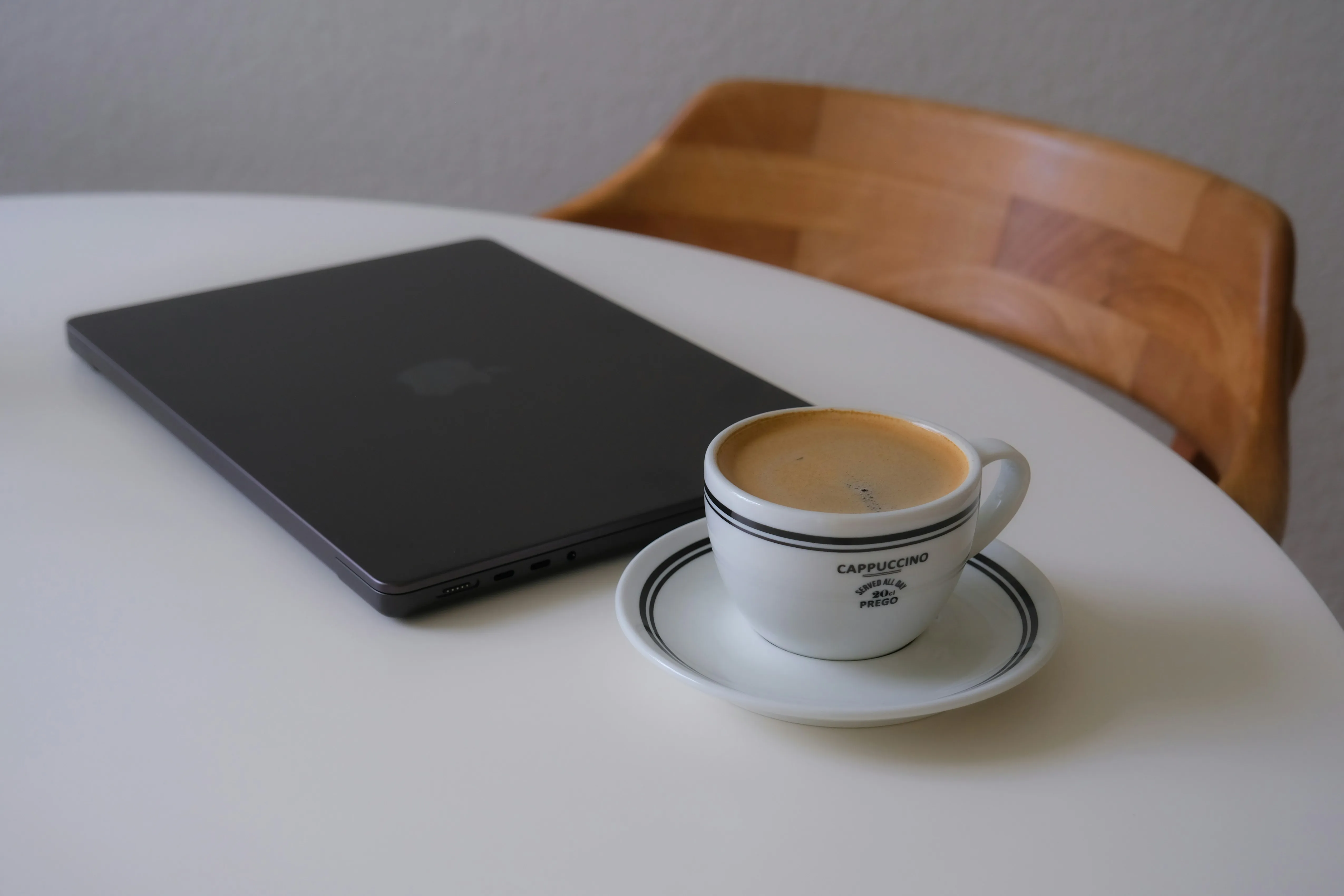 Laptop and coffee mug on a desk. A wooden chair is tucked into the desk. Photo by @Ubeyonroad form Unsplash