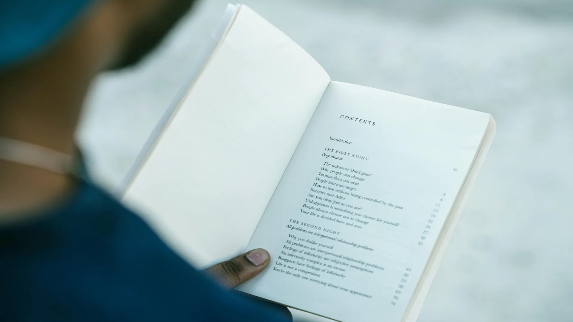 Person holding a book open to the table of contents.
